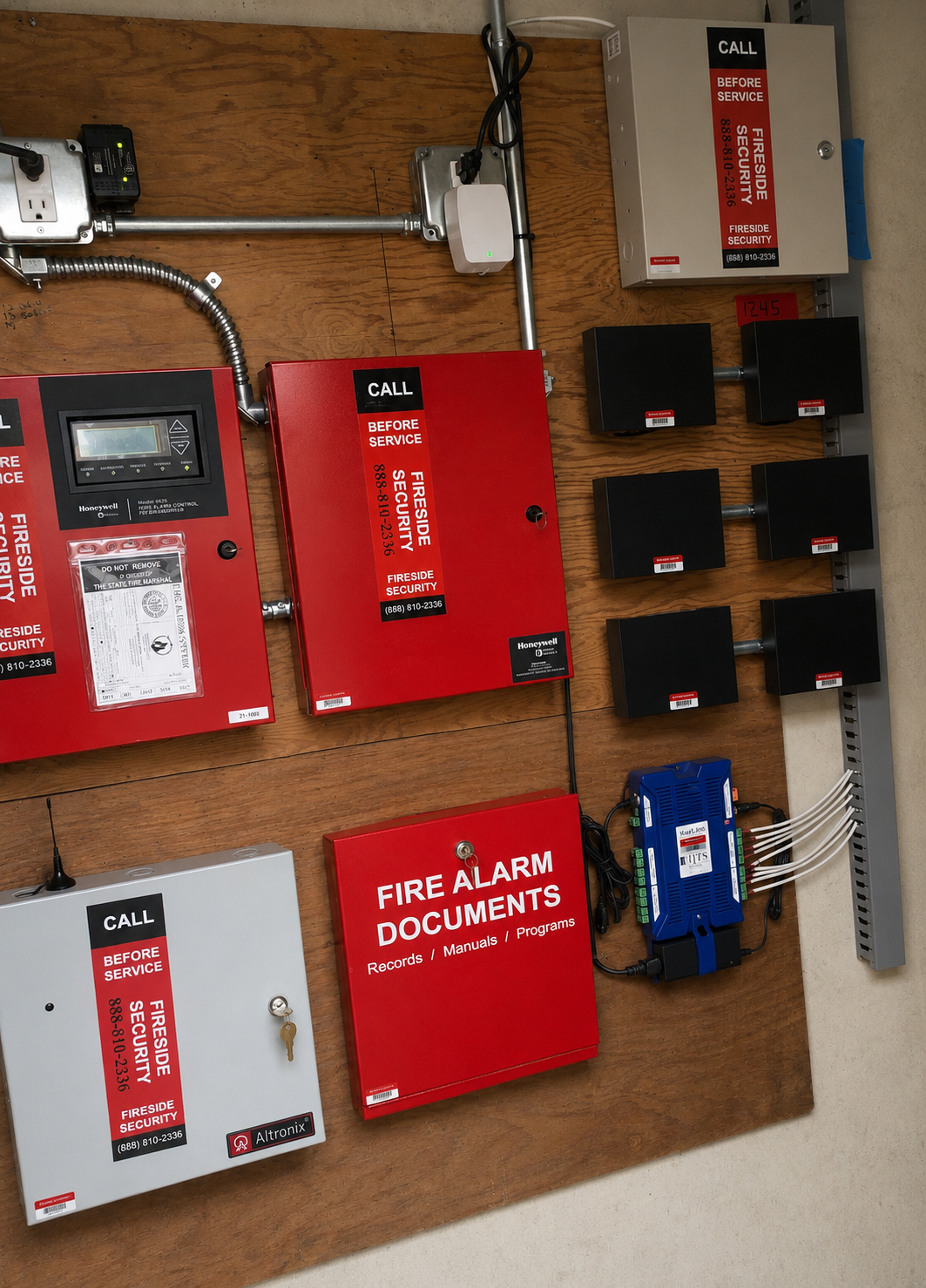 Fireside Security fire alarm and access control installation — Honeywell FACP with state fire marshal tag, Altronix power supply, network head-end, and Fireside-branded 'Call Before Service' enclosures on a commercial backboard